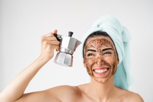 Jeune femme souriante appliquant un masque de gommage au café sur le visage